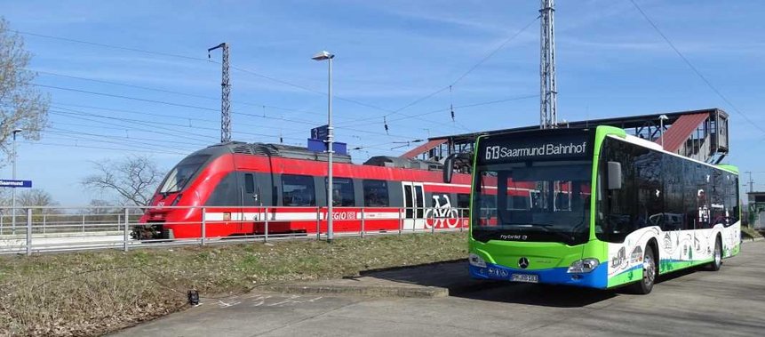 Das Foto zeigt einen Zug und einen Bus nebeneinander am Bahnhof Saarmund.