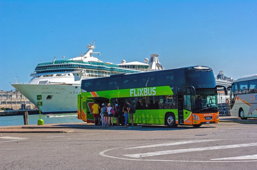Das Foto zeigt einen Flixbus am Hafen von Venedig, im Hintergrund ein großes Fahrgastschiff.