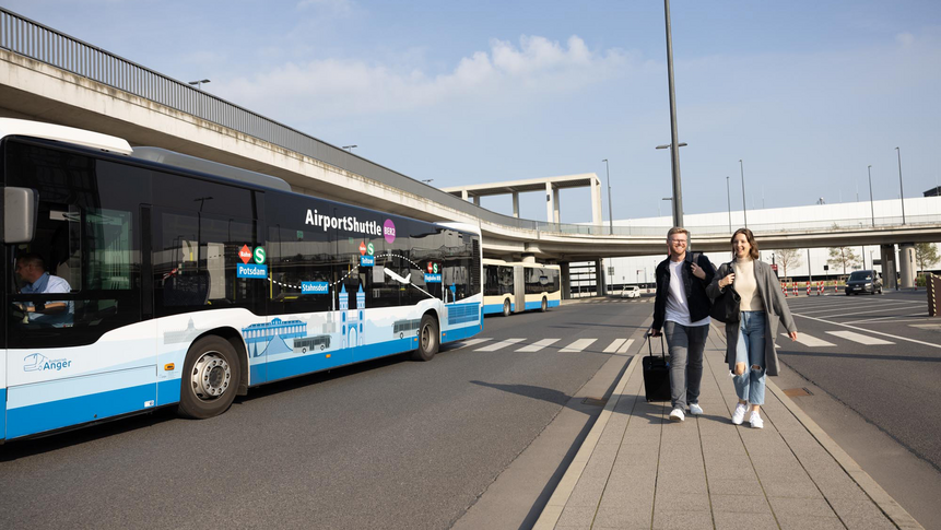 Das Foto zeigt zwei Personen mit Gepäck vor dem Eingang des Flughafens BER.
