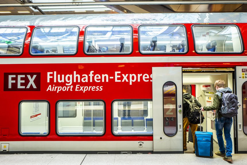 Das Foto zeigt Personen mit Gepäck, die in einen Zug zum Flughafen BER einsteigen.